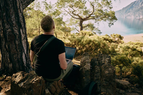 A traveler using a laptop outdoors, surrounded by maps and travel guides.