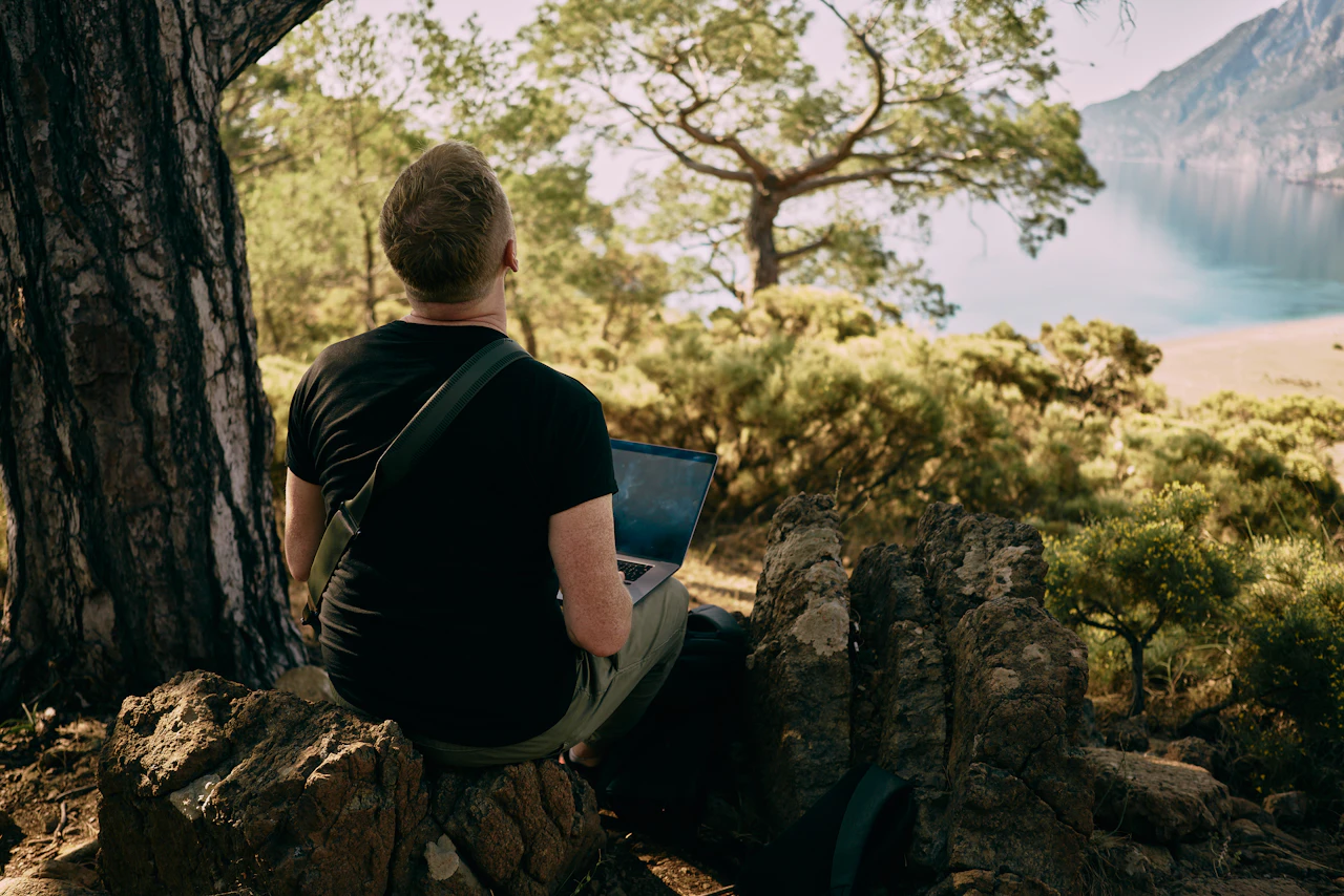 Man sitting on a rock working on a laptop outdoors
