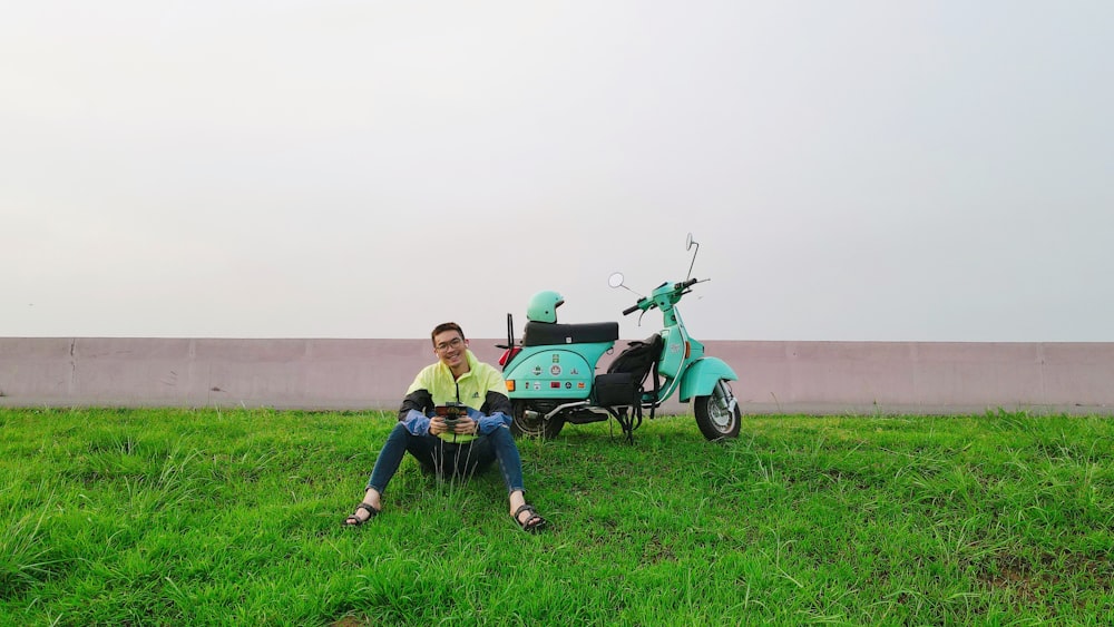 a man sitting in the grass next to a scooter