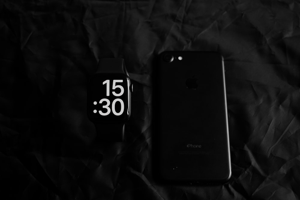 a black cell phone sitting next to a black clock