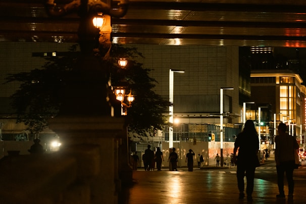 An urban street scene at dusk with people walking under glowing streetlights, capturing everyday life.