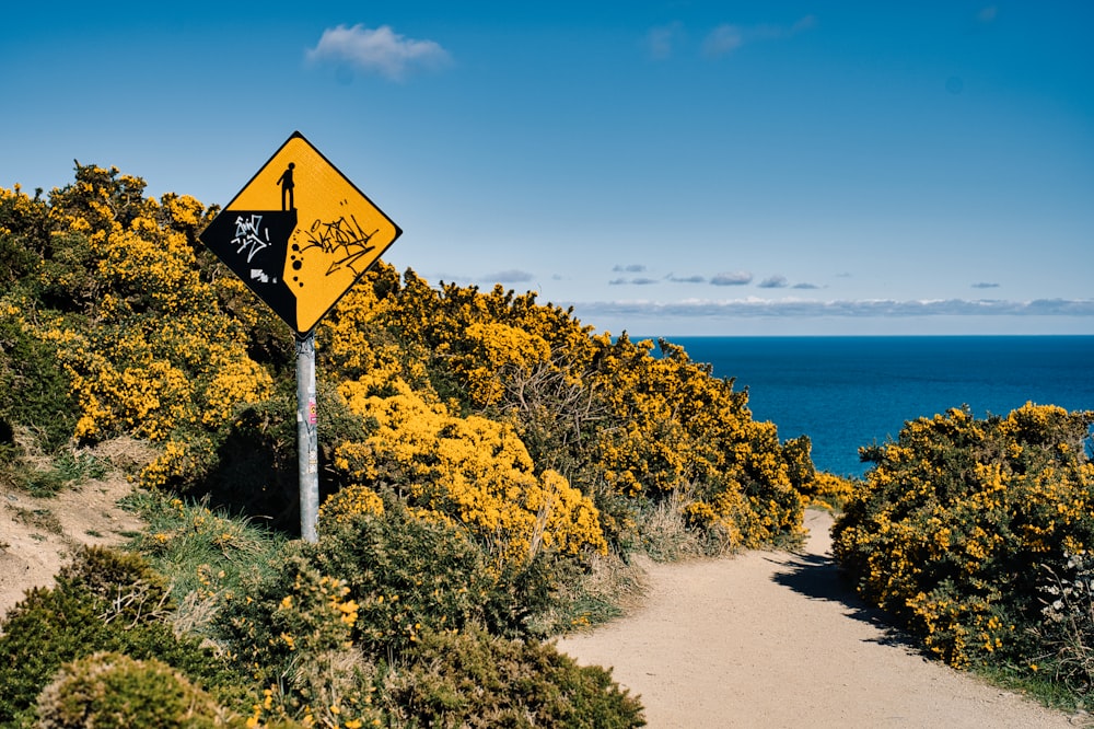 a yellow street sign sitting on the side of a lush green hillside