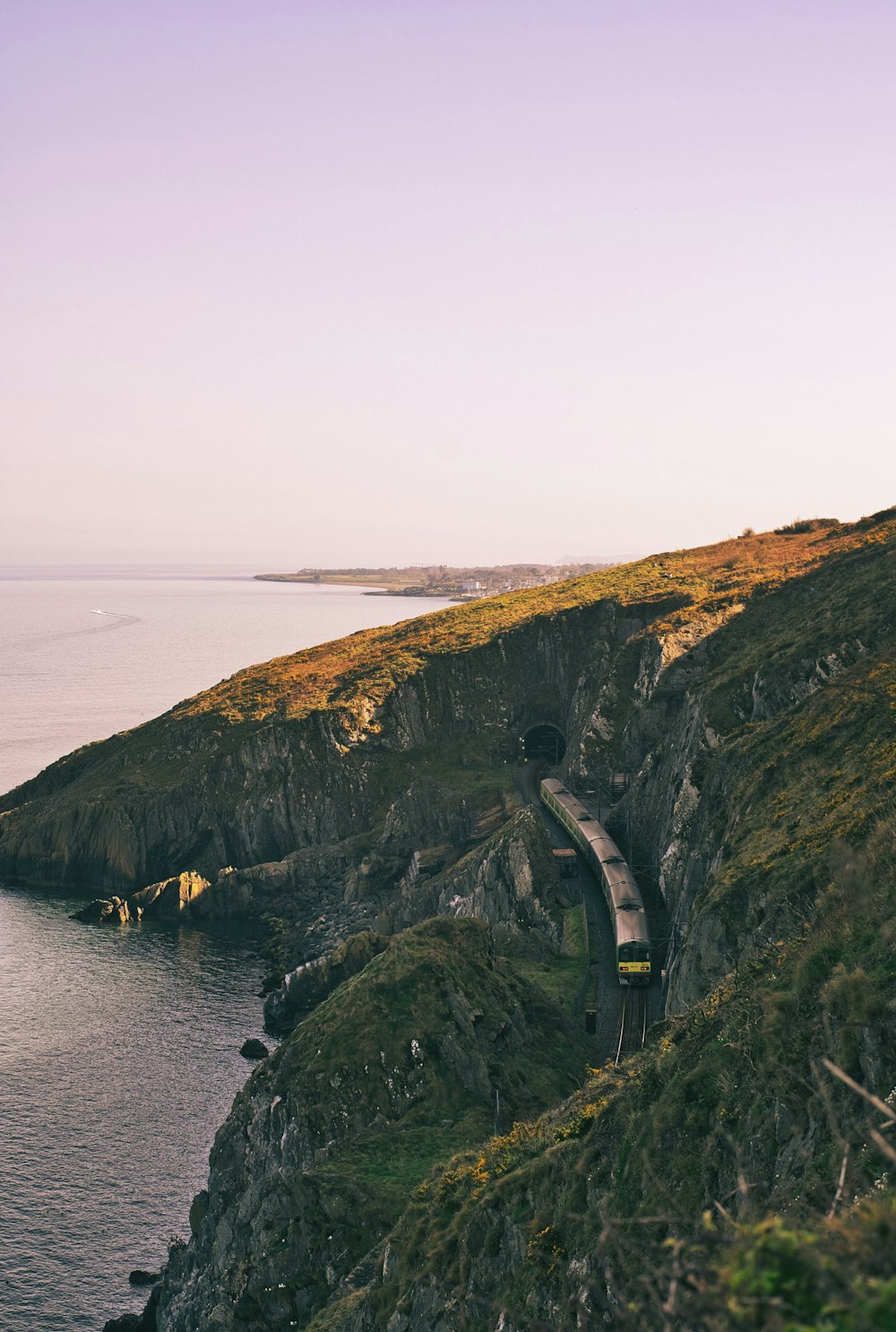 a train traveling along the side of a cliff next to the ocean