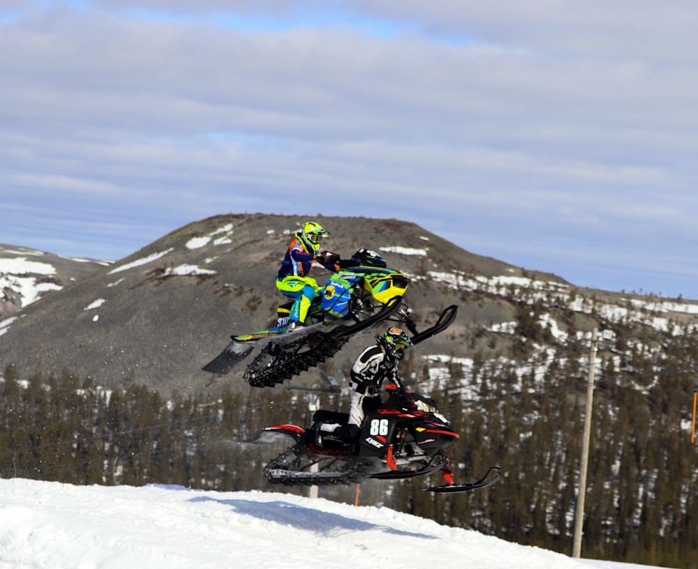 two people on snowmobiles doing tricks in the air