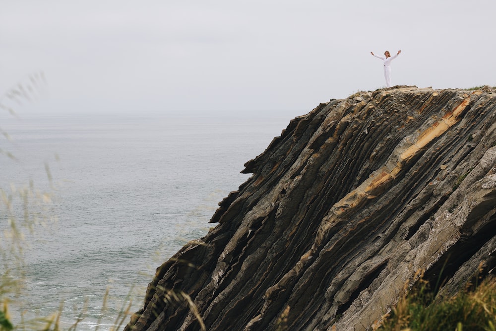 a man standing on top of a cliff next to the ocean