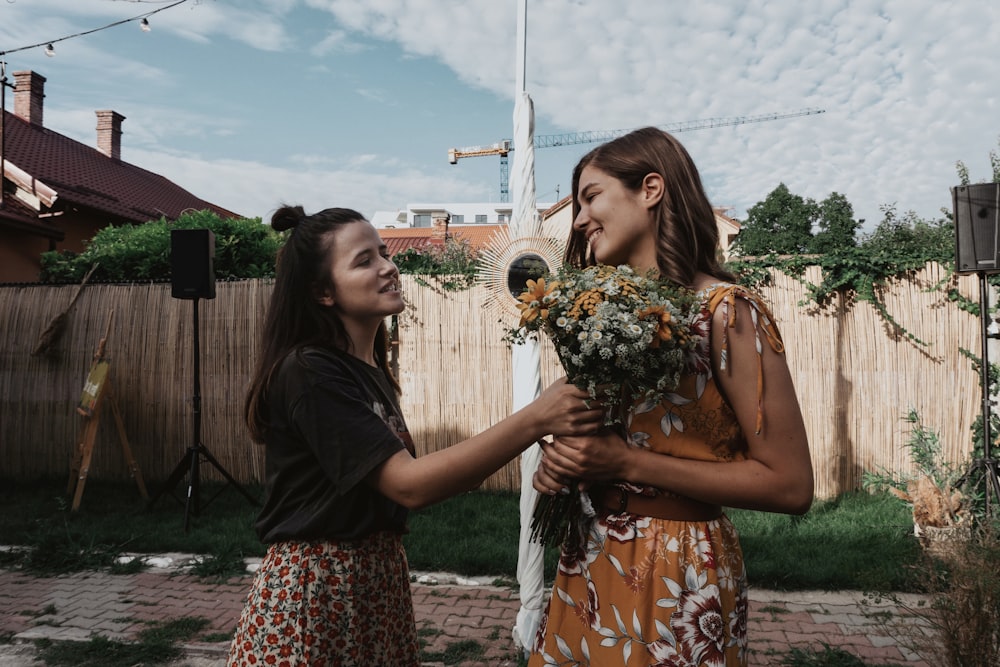 two women standing next to each other holding flowers