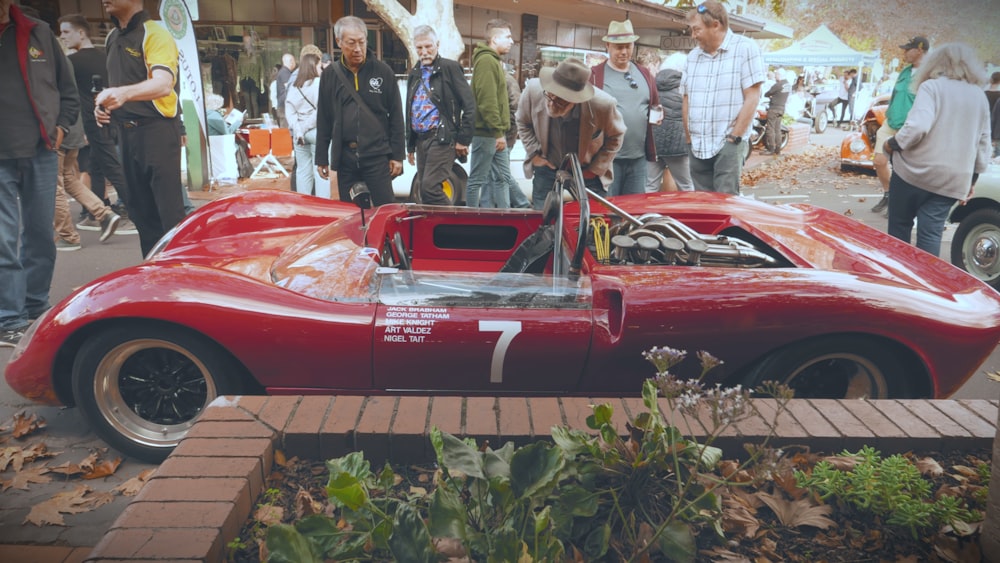 a group of people standing around a red race car