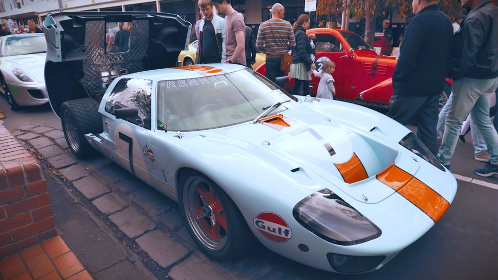 a group of people standing around a white and orange race car