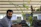 A man in an office surrounded by plants, working on a laptop with a family tree displayed.