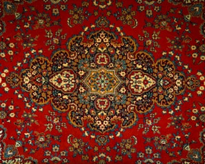 An intricate and detailed Persian rug features a central medallion with ornate floral and geometric patterns. The design is symmetrical and rich in detail, showcasing a traditional style with elaborate motifs.