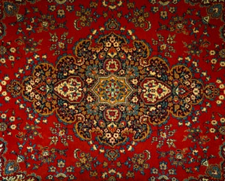 An intricate and detailed Persian rug features a central medallion with ornate floral and geometric patterns. The design is symmetrical and rich in detail, showcasing a traditional style with elaborate motifs.