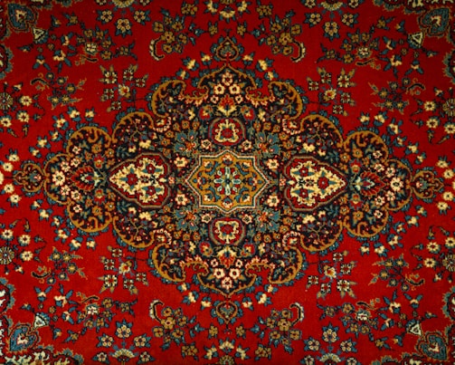 An intricate and detailed Persian rug features a central medallion with ornate floral and geometric patterns. The design is symmetrical and rich in detail, showcasing a traditional style with elaborate motifs.