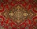 An intricate and detailed Persian rug features a central medallion with ornate floral and geometric patterns. The design is symmetrical and rich in detail, showcasing a traditional style with elaborate motifs.