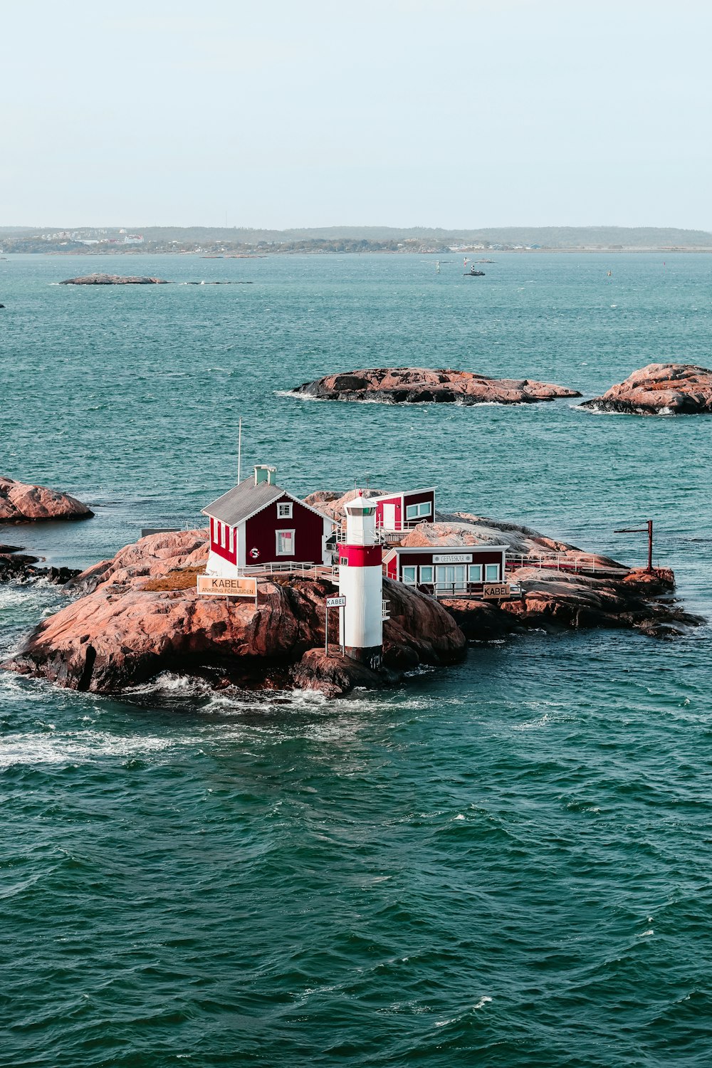 a red and white house sitting on top of a rock in the ocean