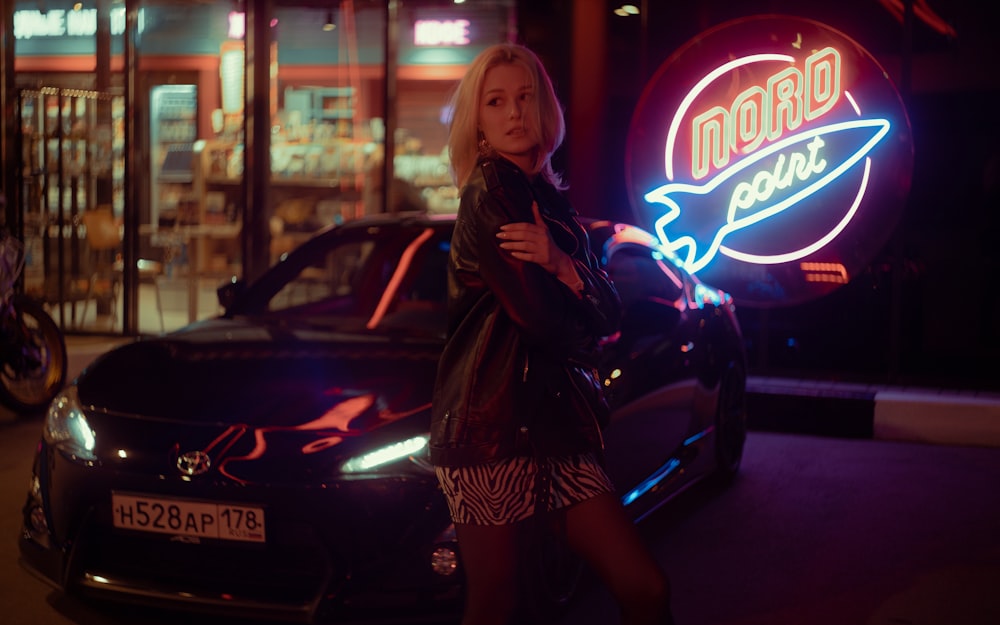 a woman standing next to a car in front of a neon sign
