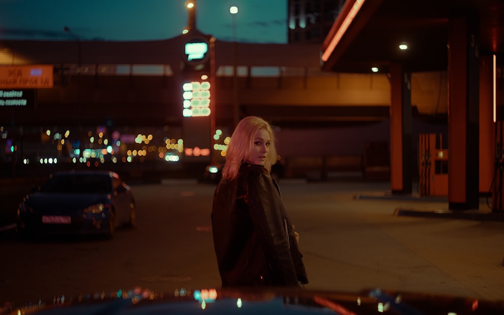 a woman with pink hair standing in front of a gas station