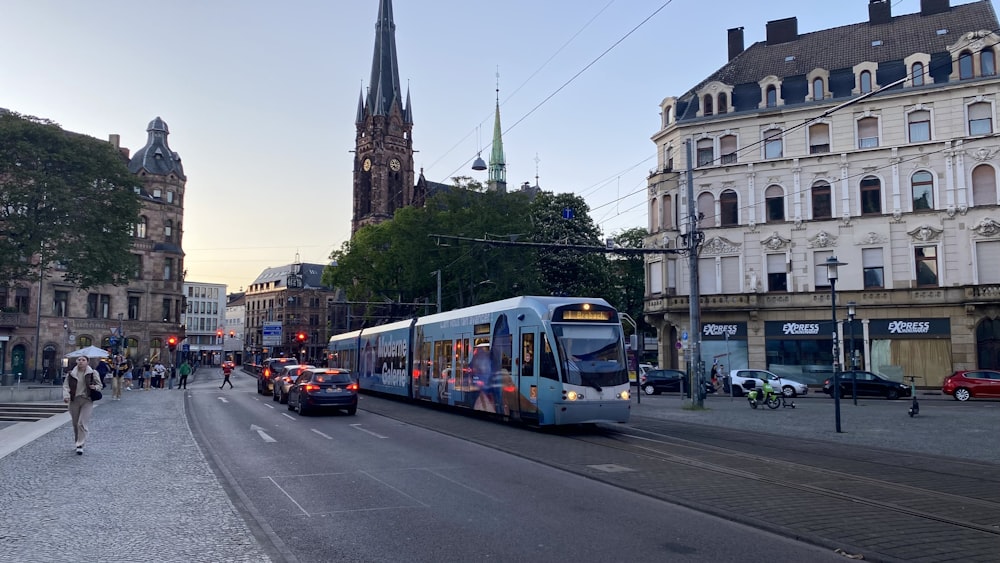 a blue and white train traveling down a street next to tall buildings