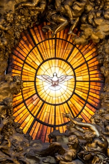 A warmly lit stained glass window depicting a dove symbolizing the Holy Spirit.