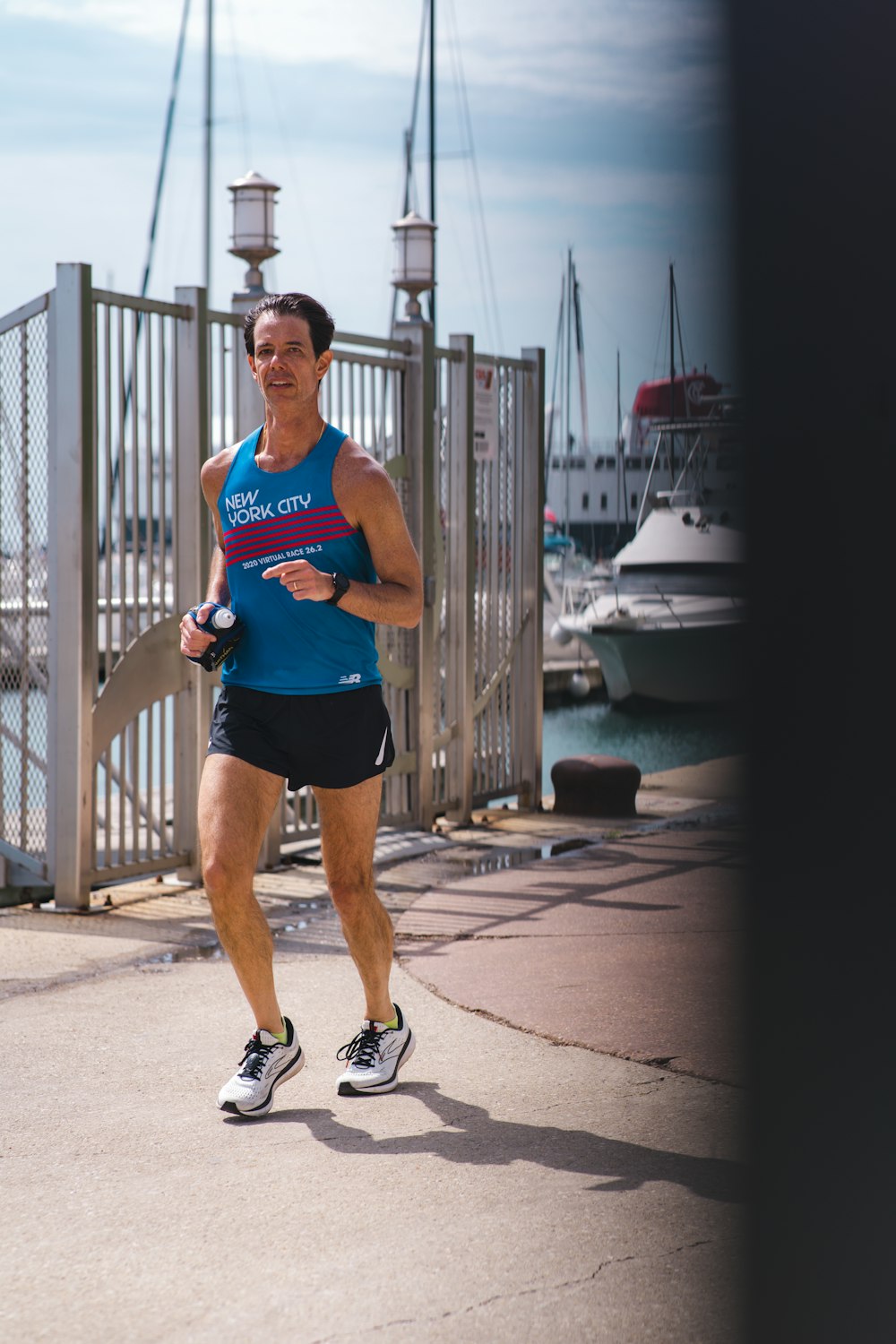 Un hombre corriendo por una acera junto a un puerto deportivo