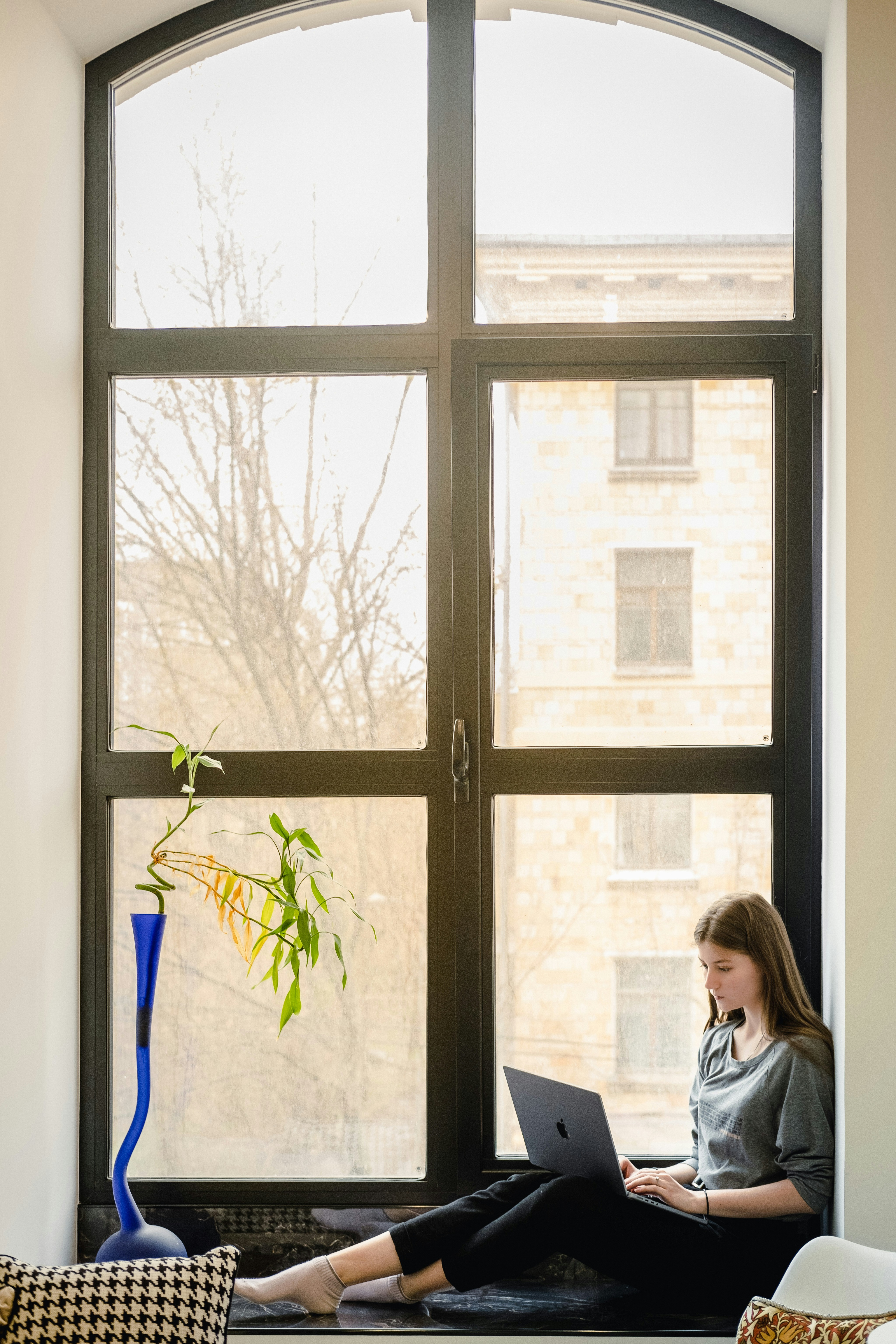 a woman sitting on a window sill using a laptop