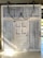 A large wooden sliding barn door with metal corrugated panels, set on a rail system. The door features visible chains and metal hardware, creating a rustic and industrial appearance. It has a smaller door within its structure.