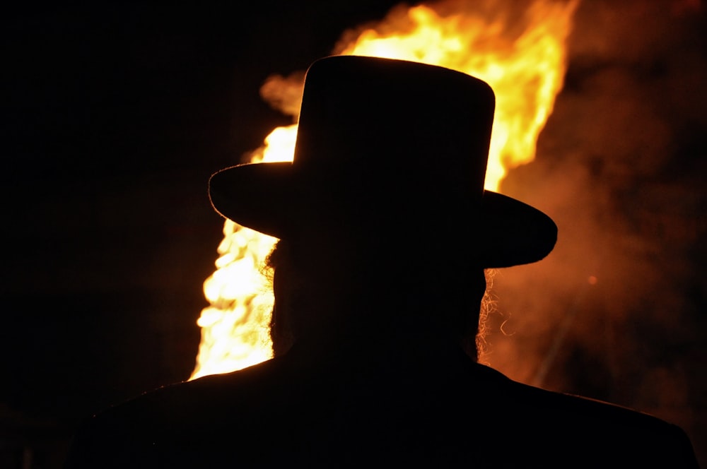 a silhouette of a man wearing a top hat in front of a fire