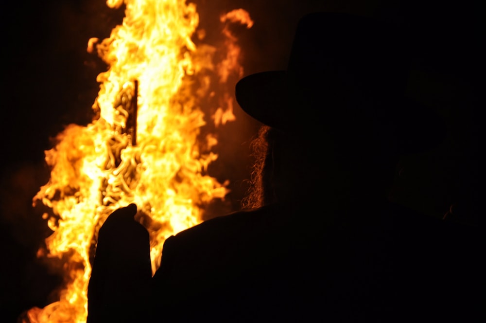 a man in a hat standing in front of a fire