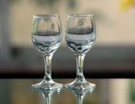 Pair of wine glasses resting close on a polished marble table, with faint reflections and a blurred silhouette behind.