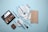 A flat lay of makeup products including a beige wallet, an eyeshadow palette, various makeup brushes with light blue handles, a compact, and a red lipstick all arranged on a light blue background.