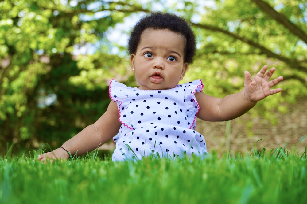 a baby girl sitting in the grass with her hands out