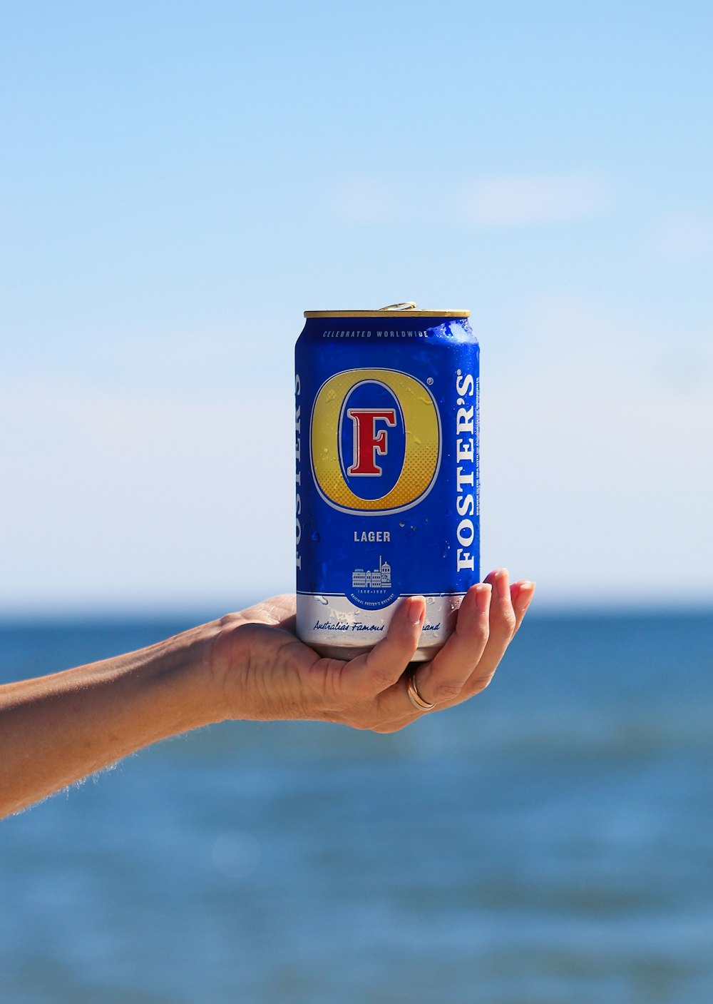 a hand holding a can of beer in front of a body of water