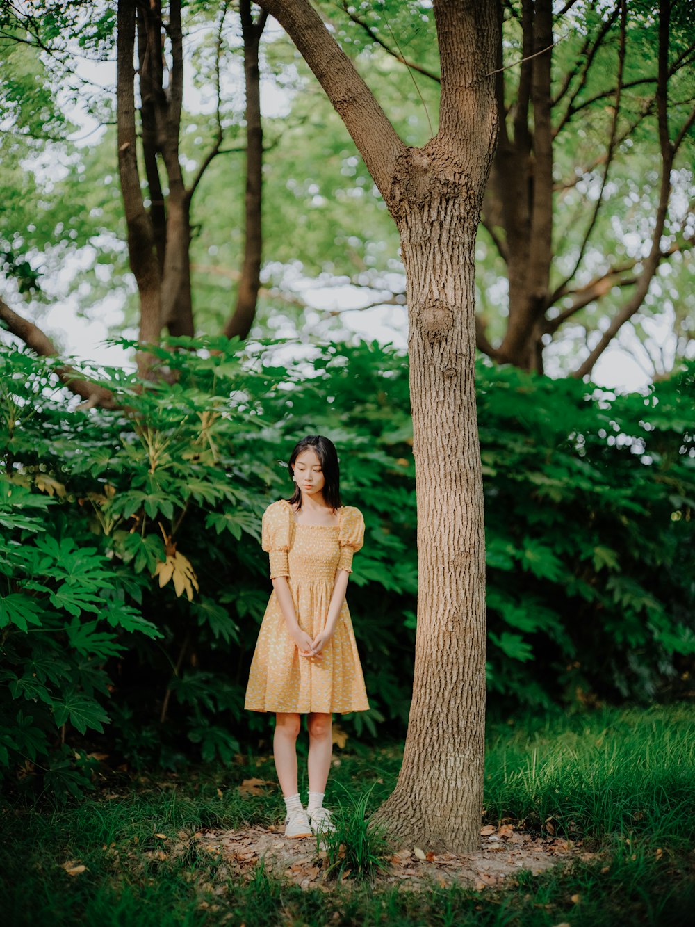 a woman in a yellow dress standing next to a tree