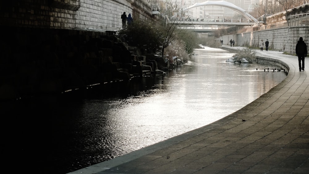 a man walking down a sidewalk next to a river