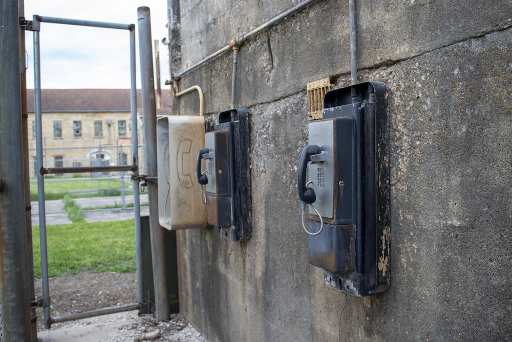 two old telephones are attached to a concrete wall