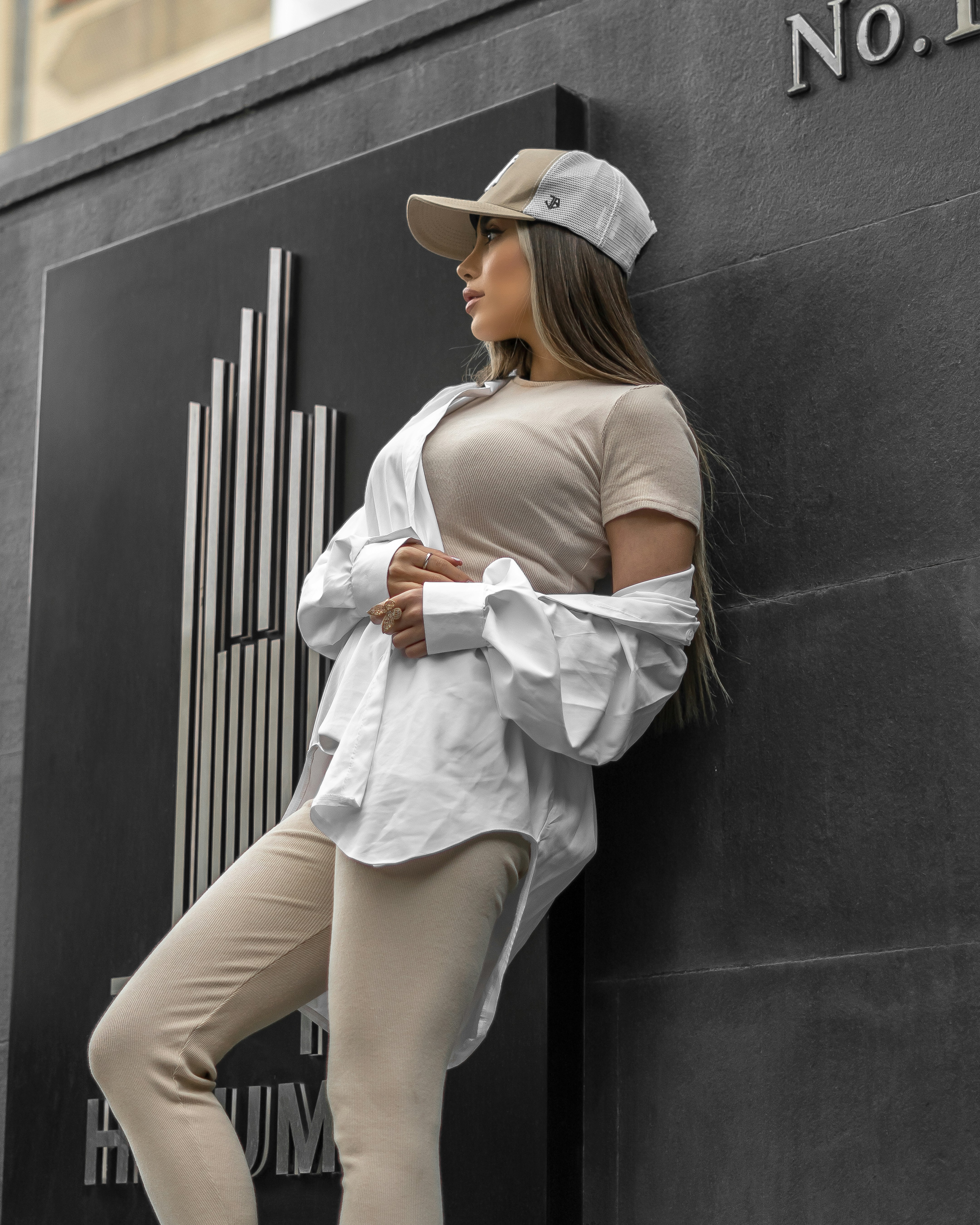 a woman leaning against a wall wearing a hat