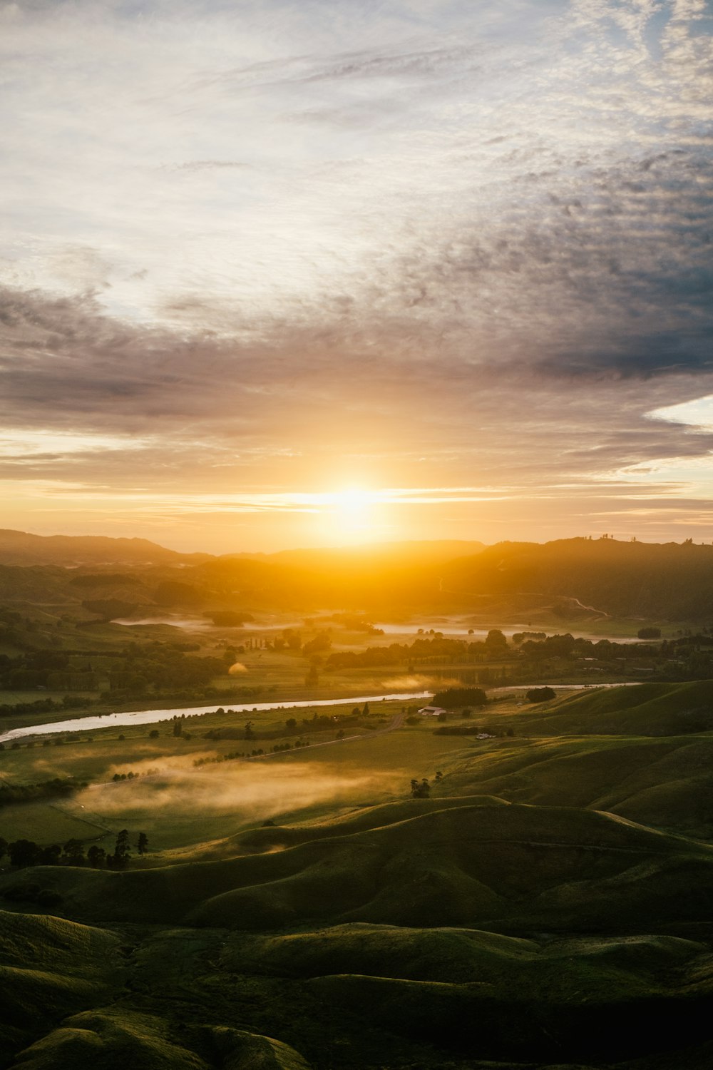 El sol se está poniendo sobre un valle con un río que lo atraviesa