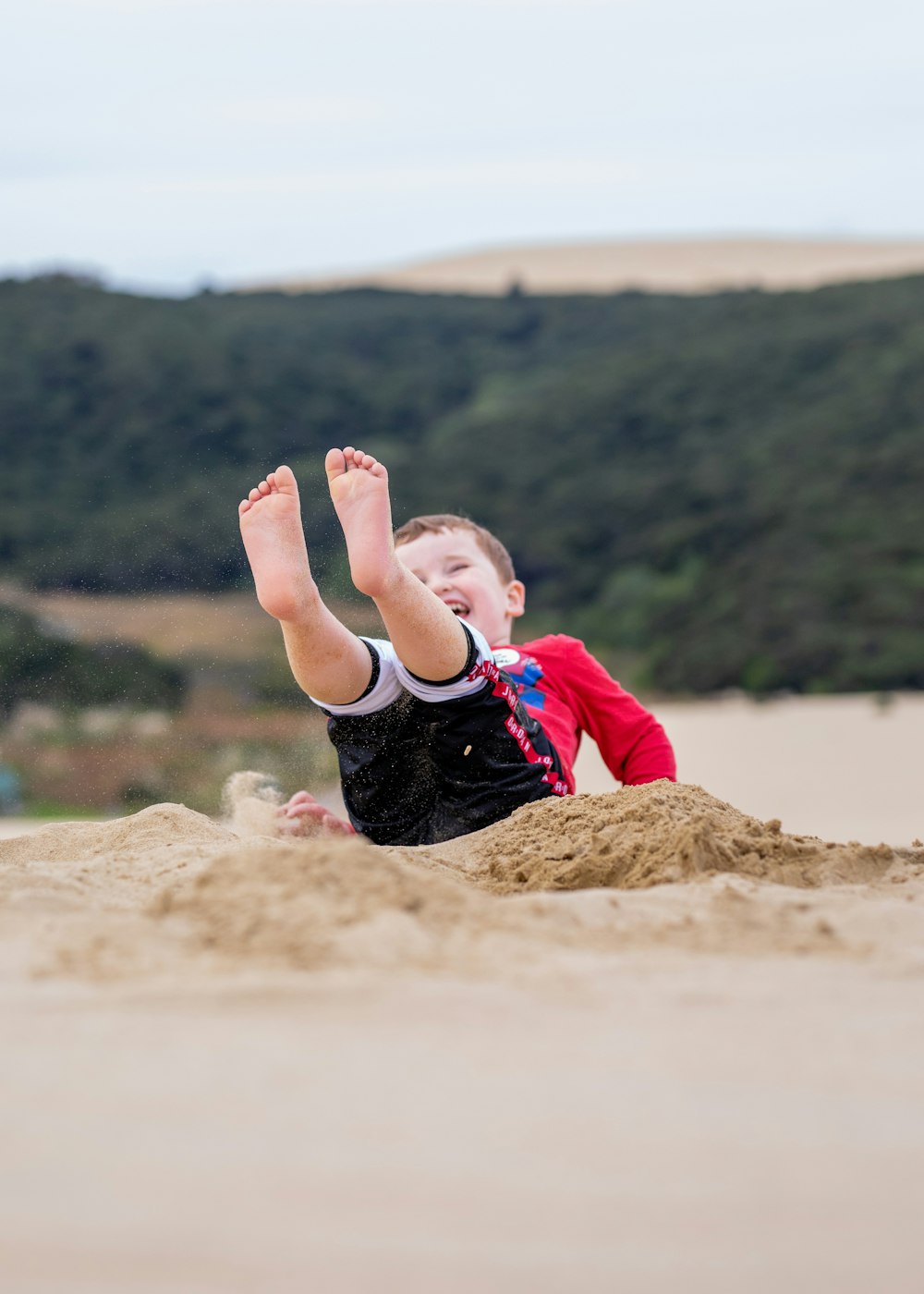 a young boy laying on top of a sandy beach