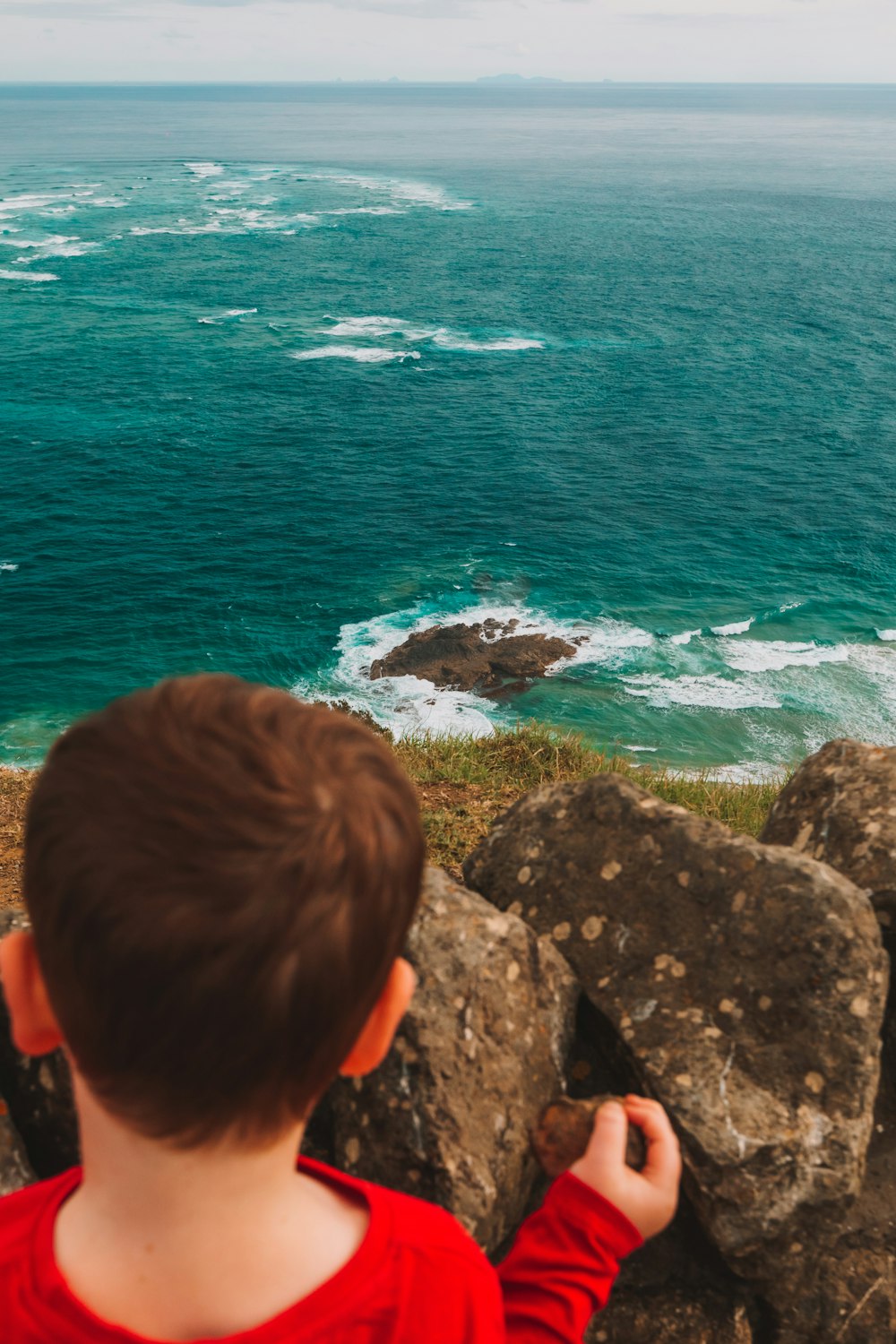 a young boy standing on top of a cliff next to the ocean