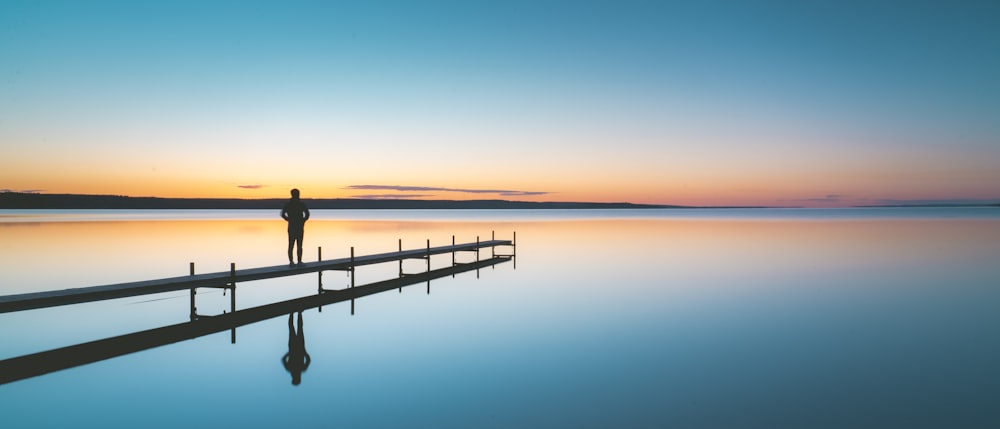 a person standing on a dock at sunset