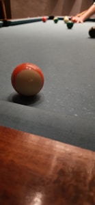 A close-up view of a pool table with several billiard balls resting on the green felt surface. A hand is visible in the background, poised to take a shot.