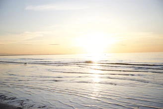 A tranquil seascape at sunset with gentle waves reflecting warm golden hues.