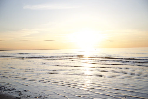 A tranquil seascape at sunset with gentle waves reflecting warm golden hues.
