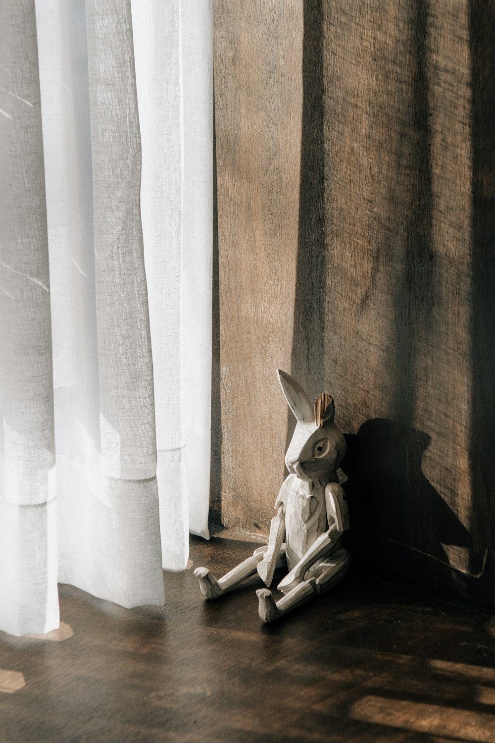 a white rabbit sitting on the floor next to a curtain