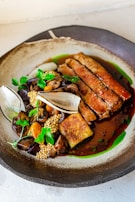 A beautifully plated gourmet dish featuring slices of roasted meat, garnished with fresh parsley and accompanied by a variety of vegetables and grains. The dish is presented on an elegantly designed plate with subtle gradients of brown and green.