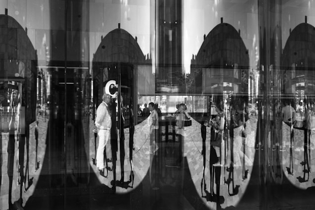A complex interplay of reflections and silhouettes is created by glass, showcasing a group of people in various postures. The reflections cause a distortion, leading to an intriguing pattern of repeated shadows and shapes.