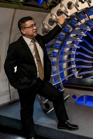A man in a suit and tie is posing next to a large industrial turbine or engine component. The setting appears professional and technical, with a focus on machinery.