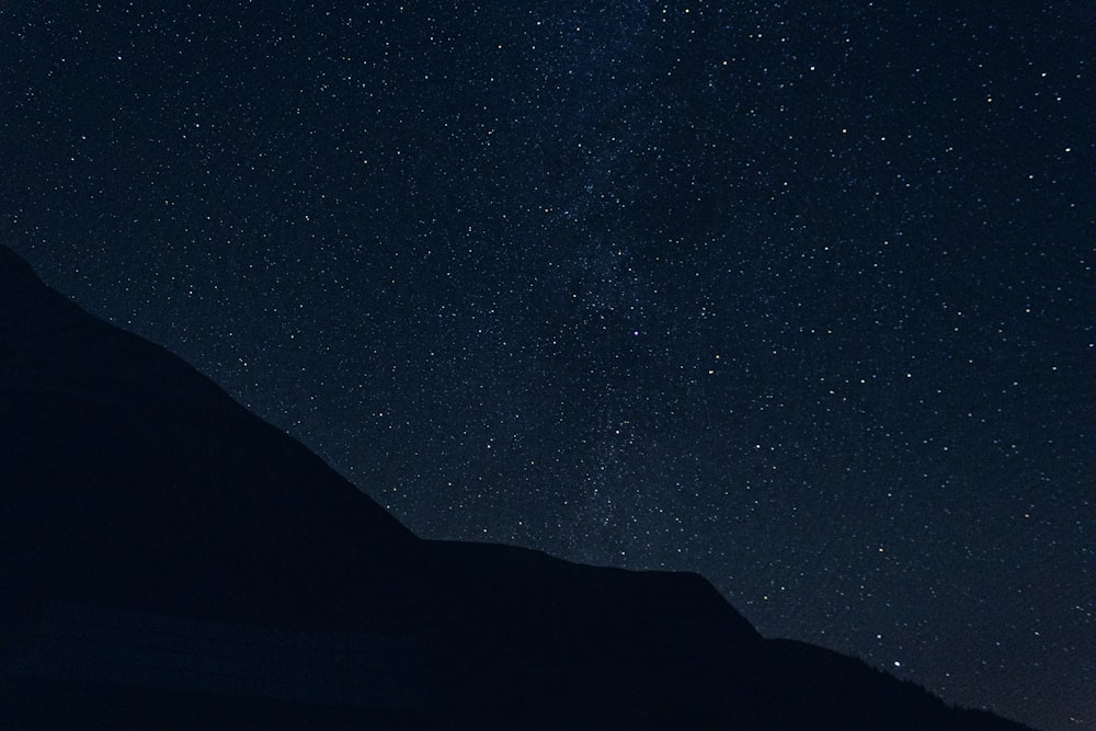 the night sky with stars above a mountain