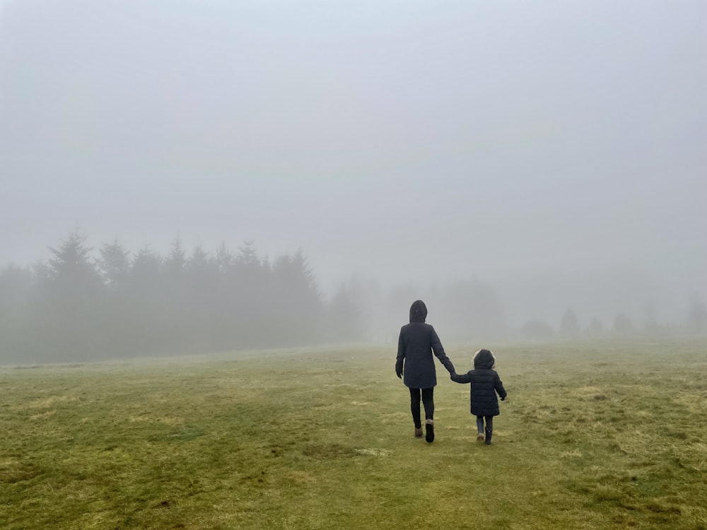 a woman and a child walking through a foggy field
