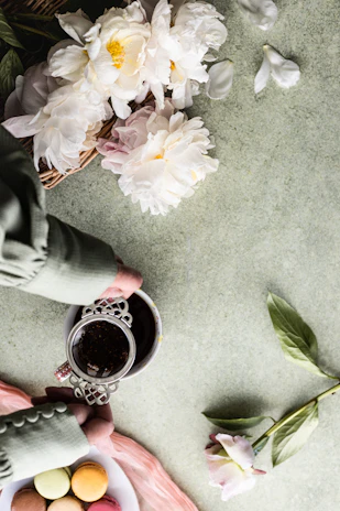 Close-up of hands holding a cup of tea with pink flowers in the background.