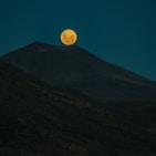 a full moon rising over a mountain range